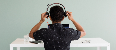 Person sitting at a desk with headphones on, facing a computer screen.
