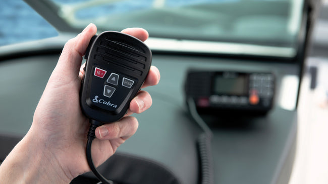 Hand holding a Cobra mic attached to a mounted marine radio
