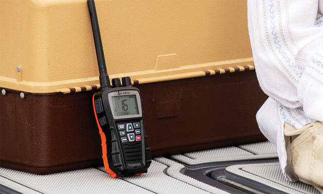 Handheld marine radio device leaning up against at tacklebox on a boat deck